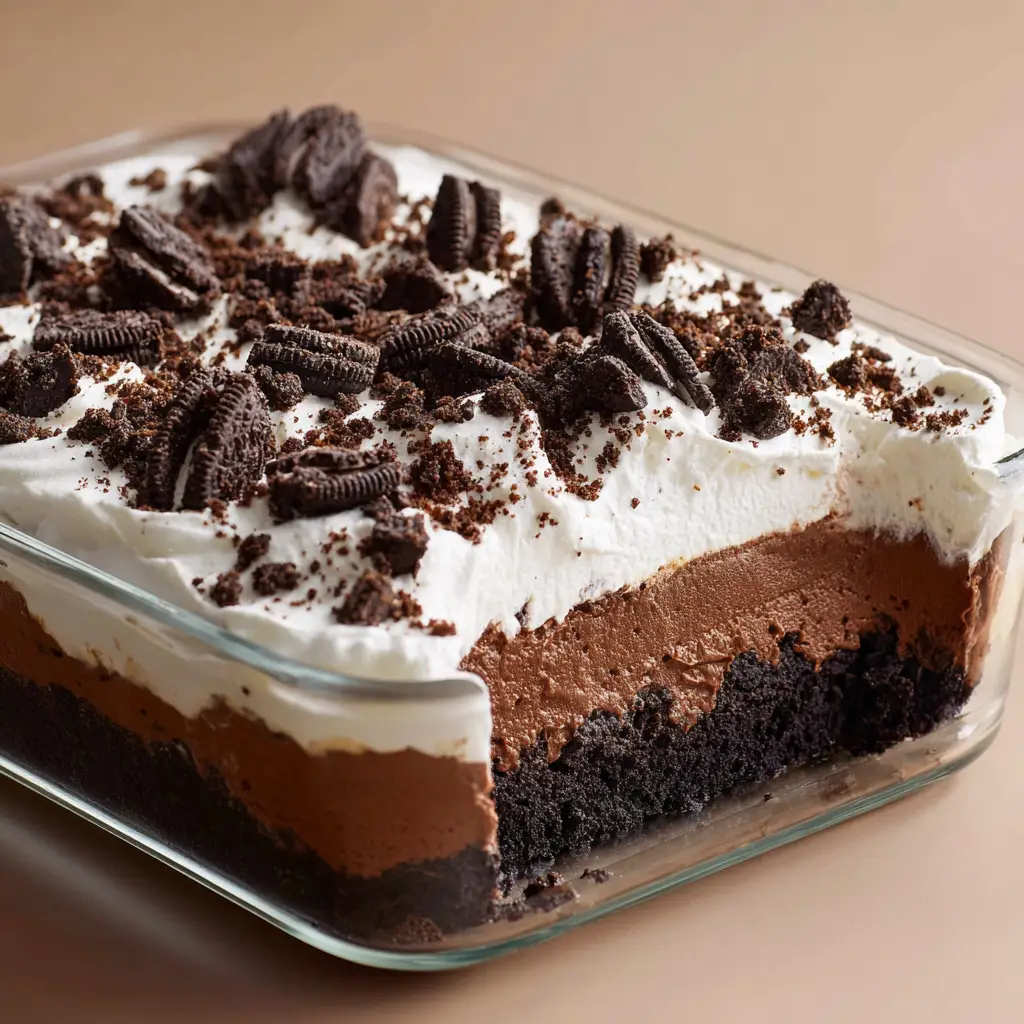 Close-up of the thick chocolate pudding layer being spread cleanly over the dense white cream cheese filling in a glass dish.