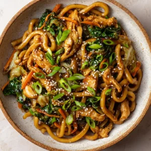 An overhead view of a serving of homemade Yaki Udon in a speckled ceramic bowl, showcasing the tender chicken and vibrant vegetables. (Yaki Udon Recipe)