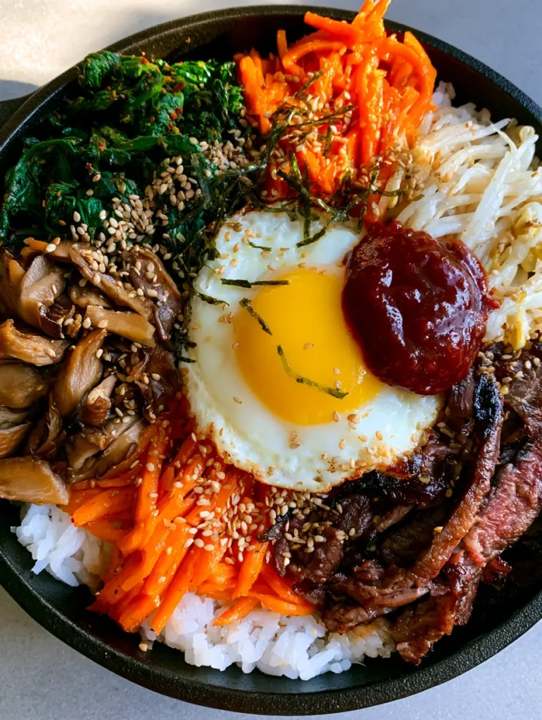 Bibimbap Recipe served in a black pan featuring toasted sesame seeds and dried seaweed slivers garnish.