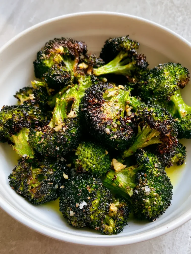 Side view of air fried broccoli florets showing the olive oil shimmer and minced roasted garlic bits. (Air Fryer Broccoli)