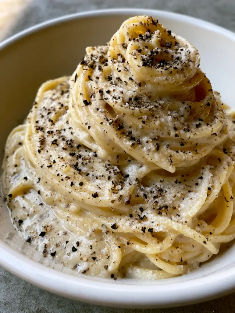 Close up of glossy, pale-cream colored sauce on spaghetti speckled with coarse cracked black pepper for Authentic Cacio e Pepe.