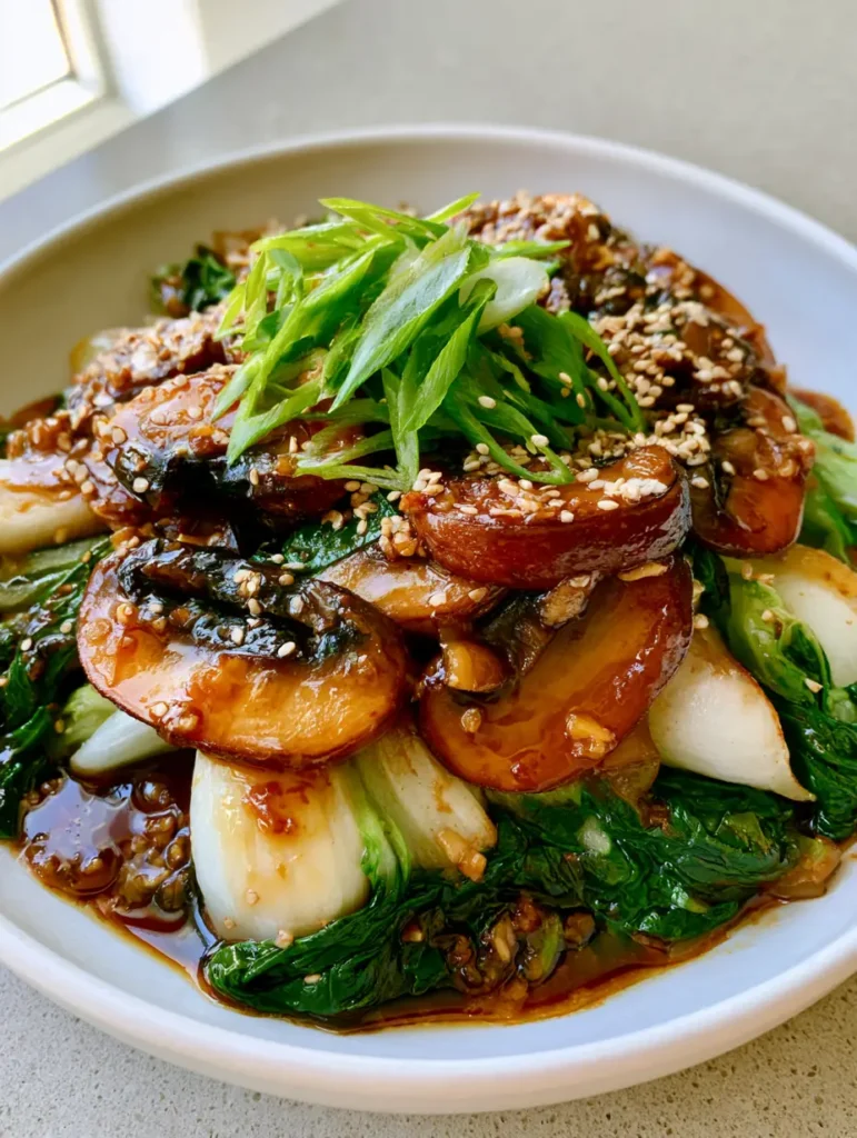 Close-up of seared cremini mushrooms and vibrant green baby bok choy in a glossy sauce. (Bok Choy and Mushroom Stir Fry)