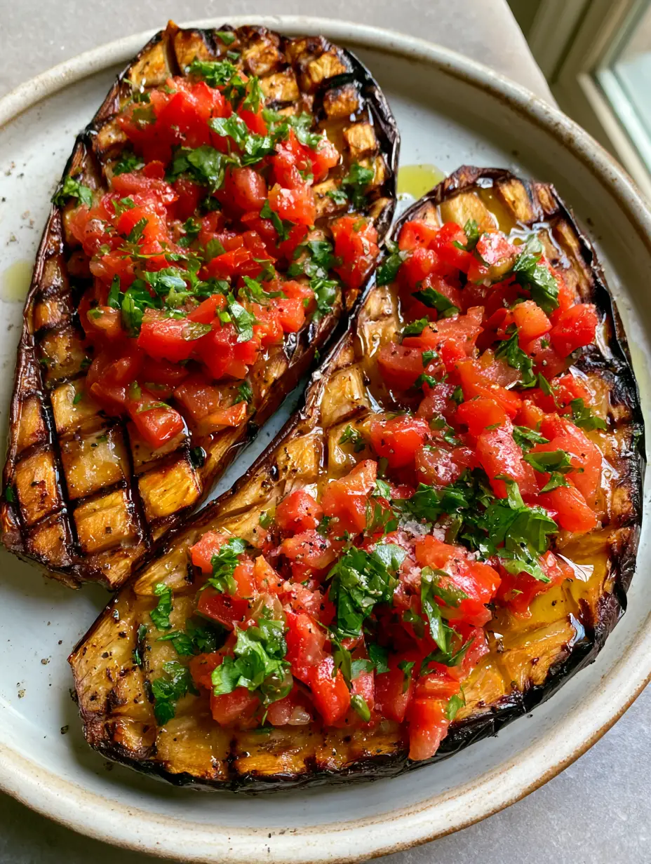 Mediterranean Roasted Eggplant with Garlic and Fresh Tomato Topping 4 A handheld smartphone photo of Mediterranean Roasted Eggplant halves on a rustic ceramic plate.