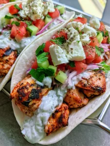 A handheld smartphone photo of Mediterranean Chicken Tacos on a grey stone surface. (Mediterranean Chicken Tacos)